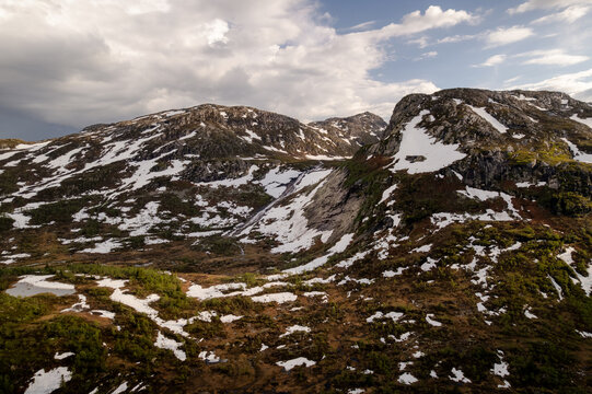Aerial view of rugged, snow-dusted mountains under a dramatic sky where light and shadow dance across the landscape, Dalen, Telemark, Norway.