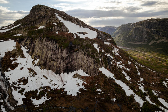 Aerial view of a rugged mountain peak with patches of snow clinging to its steep slopes, contrasting against the dark rock face, Dalen, Telemark, Norway.