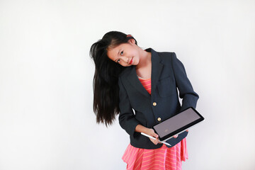 Confident young girl in business suit holding digital tablet and stylus, smiling brightly while tilting her head playfully against white background.