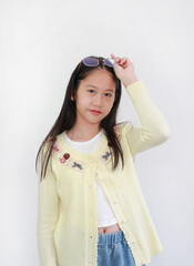 A cute young Asian girl in a yellow cardigan and jeans against white background is posing while...