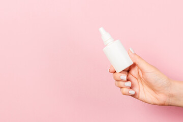 Female hand holding cream bottle of lotion isolated. Girl give tube cosmetic products on pink background