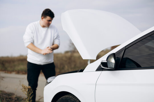 Young man inspecting electric car by roadside