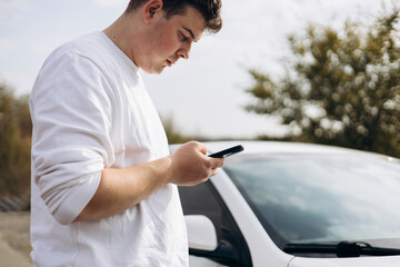 Young man using phone next to electric vehicle