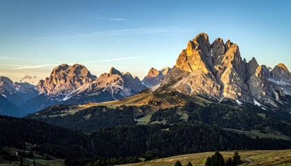 A panoramic view of jagged mountain peaks illuminated by the warm glow of sunset, set against a clear blue sky.