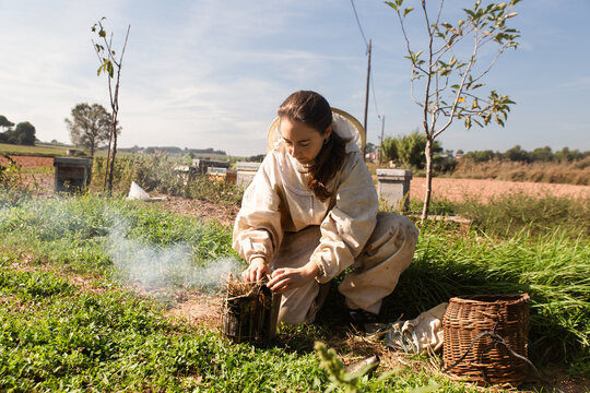 Female Beekeeper Preparing Smoker in Rural Apiary Field