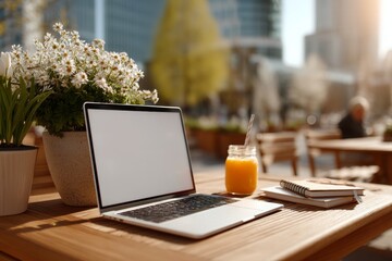Laptop with blank screen on outdoor cafe table with juice and notebook sunny day urban freelancer style