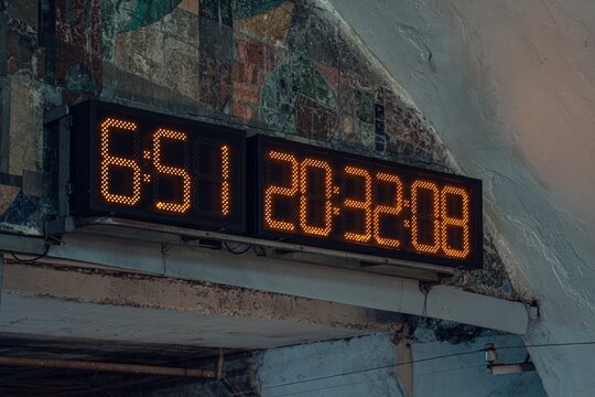 A close-up view of a digital clock showing time and a numeric display, set against a textured wall with colorful patterns.