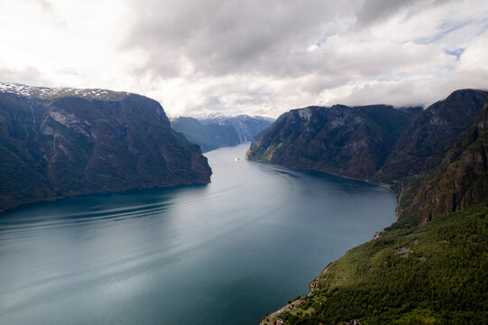Aerial view of the majestic fjord cuts through towering cliffs, reflecting the cloudy sky in its deep waters, a silent dance of nature's grandeur, Aurland, Vestland, Norway.