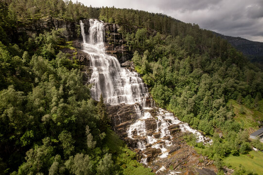 Aerial view of the cascading Tvindefossen waterfall plunges down the rocky cliffside amidst lush green trees, Skulestadmo, Vestland, Norway.