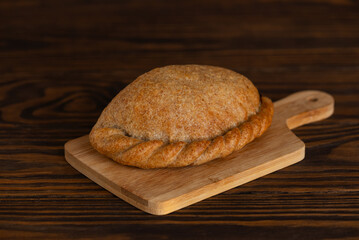 Baked cabbage pie on a wooden board on a brown table. Russian baked puff pastry with cabbage fillings.