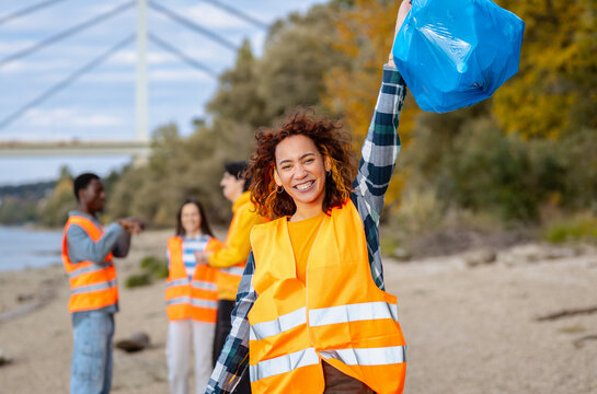 Portrait of smiling female volunteer in a safety vest holding trash bags during a community environmental cleanup event.