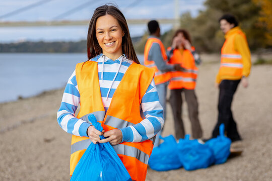 Portrait of smiling female volunteer in a safety vest holding trash bags during a community environmental cleanup event.