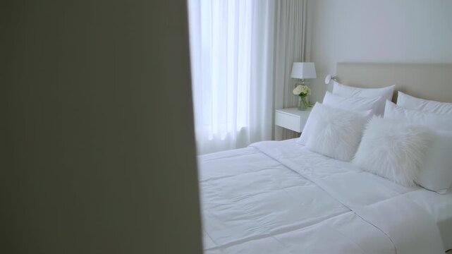 Bright, airy bedroom with white bedding, sheer curtains, side table with lamp, and floral arrangement