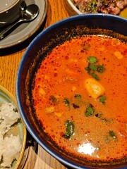 Thai tom yum soup with rich red broth herbs, and coconut base served in a blue bowl. Perfect stock photo for restaurant menus, food packaging, advertising campaigns.