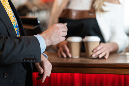 A businessman pays for takeaway coffee with his card while the barista in the cafe accepts the customers credit card during service