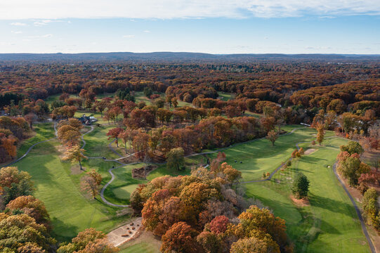 Aerial view of an emerald golf course weaves through a tapestry of autumnal trees, a blend of nature's artistry, Windsor, Connecticut, United States.