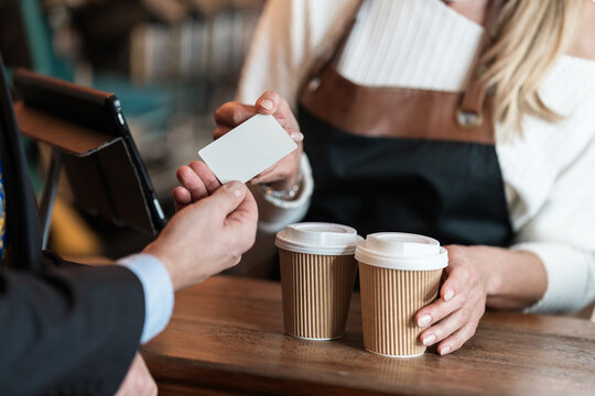 A businessman pays by card for his takeaway coffee while the cafe barista processes the customer credit card with friendly service