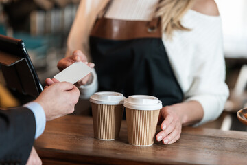 A barista in a cafe accepts a credit card as the businessman pays for his takeaway coffee showing a seamless cashless purchase