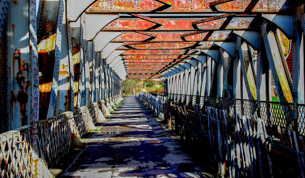 An old metal bridge with a path leading through it. - Powered by Adobe