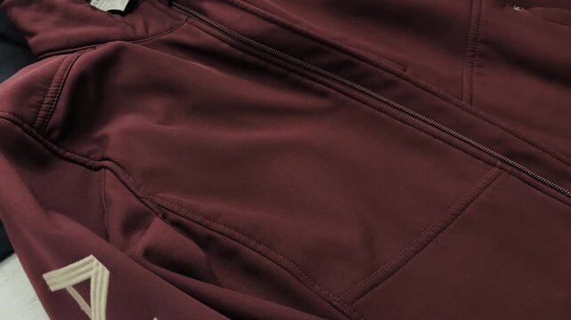 Close-up of two hands smoothing the surface of a maroon jacket laid flat, showing fabric texture and stitching details.