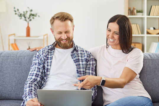 Young family couple sitting on couch together, surfing internet or watching movie. Happy husband and wife enjoying each other company, looking at screen and having fun and relaxing time at home.