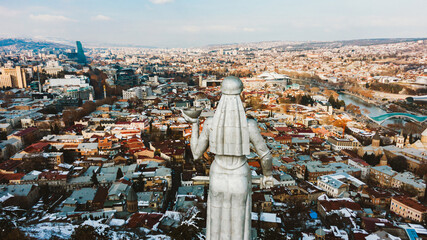 Aerial view of the back of kartlis deda, mother of georgia statue, holding a bowl of wine and a sword, overlooking the colorful cityscape of tbilisi, kura river and the bridge of peace © wifesun