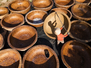 Aerial view of a worker in a conical hat stands among large, woven baskets, their textures catching the light, casting intricate shadows, Ho Chi Minh City, Ho Chi Minh City, Vietnam.
