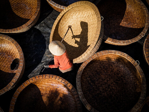 Aerial view of a woman in a conical hat amidst large woven baskets, a dance of light and shadow, creating a captivating visual narrative, Ho Chi Minh City, Ho Chi Minh City, Vietnam.