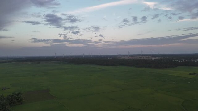 Atmospheric aerial landscape featuring a lake, green fields, wind turbines, and mountain ranges under a dramatic evening sky.