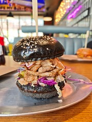Delicious gourmet burger black sesamebun, grilled meat, fresh oleslow and sauce served on a metal plate in modern restaurant. 