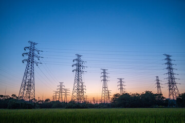Sunset behind electricity pylons and green field.
