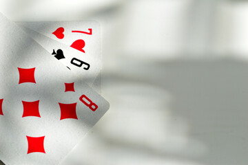 A deck of playing cards lies fanned out on a table, casting shadows from the window blinds.