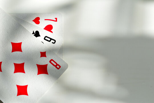 A deck of playing cards lies fanned out on a table, casting shadows from the window blinds.