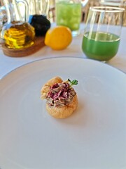 Elegant restaurant appetizer &mdash; choux pastry filled with liver p&acirc;t&eacute;, garnished with herbs and beetroot powder. Fine dining amuse-bouche served on a white plate with drinks and olive oil in the backgrou