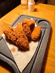 Crispy fried chicken wings in golden breading served on lavash bread over a rustic wooden board. Tasty snack, American and European comfort food close-up.