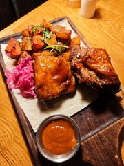Smoky barbecue pork ribs with crispy roasted potatoes, tangy pickled cabbage, and rich BBQ sauce served on a rustic wooden board. Classic American comfort food close-up.