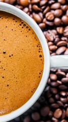 Close up of a white mug filled with frothy coffee surrounded by roasted coffee beans