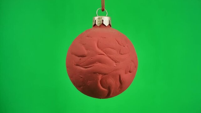 Red matte Christmas ornament with embossed swirling patterns hanging against a bright green background, metallic cap and string visible.