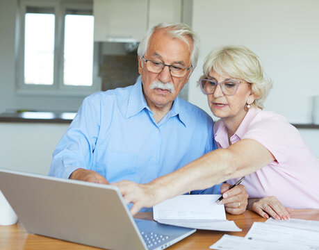 Senior couple checking bills and calculating expenses using a laptop at home, debt taxes concept, worried married elderly couple
