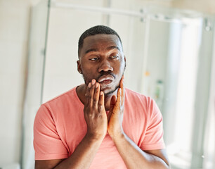 Portrait of a beautiful young black man applying beauty cream on his face skin in front of mirror in bathroom in the morning, beauty, cosmetics, skincare, hygiene concepts