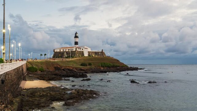 Day to night timelapse of the historic Farol da Barra, the oldest lighthouse in operation on the coast of Brazil and the Americas, in Salvador, Bahia, Brazil, zooming out. 