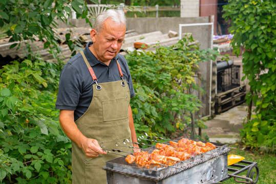 Man grilling meat outdoors in a lush garden setting