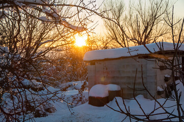 Winter sunset shines brightly over snow covered landscape and shed, creating peaceful outdoor scene for nature lovers and seasonal designs