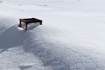 Wooden platform sits atop a snow-covered hill, surrounded by a vast expanse of white snow, reflecting bright sunlight, creating a serene winter landscape with tranquility