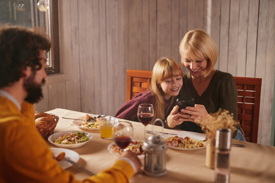 Gathered around a table, a family enjoys a warm autumn dinner filled with delicious food, happy conversation, and shared moments, while relaxing in a cozy indoor space.