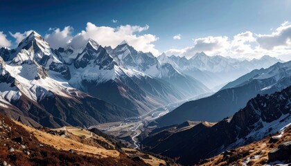 A panoramic view of a vast mountain range with snow-covered peaks, rugged slopes, and a valley below with a river and scattered vegetation.