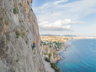 Climber scales rocky cliff with scenic coastal backdrop