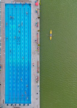 Aerial view of a vibrant blue swimming pool contrasting with the murky green water where a lone kayaker paddles, Mendoza, Mendoza Province, Argentina.