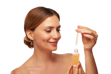 Fototapeta premium A woman with a pleasant expression holds a dropper bottle filled with a serum, preparing to apply it as part of her skincare routine, emphasizing self-care and beauty practices.