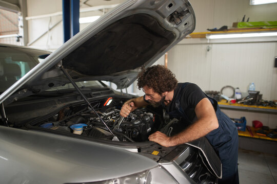 A mechanic carefully inspects and repairs the engine of a car in a well-organized auto shop, showing expertise and focus during the daytime.